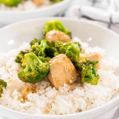 A-bowl-of-white-rice-and-Easy-Broccoli-Chicken-Stir-Fry-in-a-white-bowl-sitting-on-a-white-and-grey-kitchen-towel.