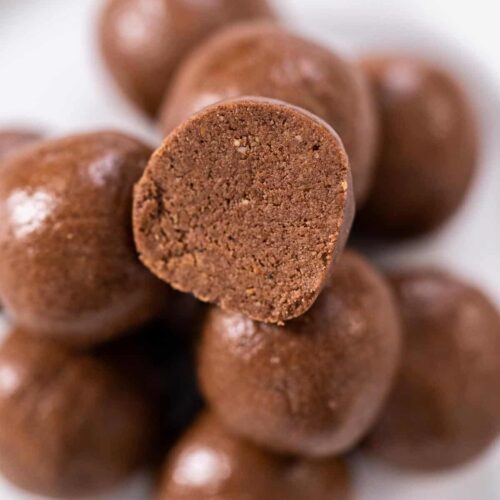 A-pile-of-chocolate-bliss-balls-with-one-cut-open-on-a-white-plate.