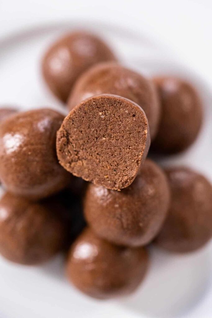 A-pile-of-chocolate-bliss-balls-with-one-cut-open-on-a-white-plate.